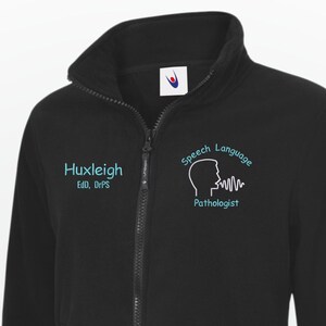 May include: Black fleece jacket with a zip-up front and a high collar. The jacket has teal text on the left chest reading "Huxleigh Ed. DPS". The right chest displays a teal graphic and the words "Speech Language Pathologist".