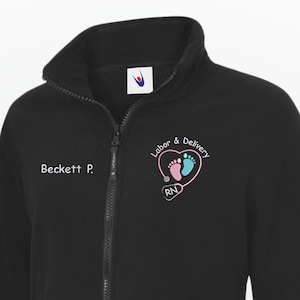 May include: Black zip-up fleece jacket with a high collar. Features the text "Beckett P." on the left chest. The right chest has a heart-shaped graphic with baby footprints and the words "Labor & Delivery" and "RN".