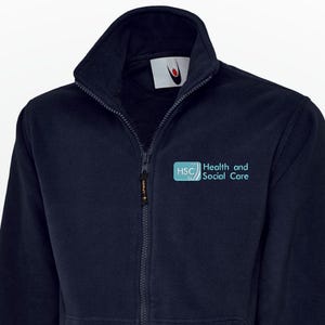 May include: Navy blue fleece jacket with a full zipper and a high collar. The jacket features two front pockets and the text "Health and Social Care" in teal. The jacket has a small logo on the upper left chest.