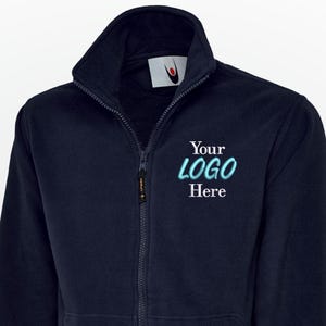 Könnte beinhalten: Marineblaue Fleecejacke mit durchgehendem Reißverschluss, zwei Vordertaschen und hohem Kragen. Der Text "Your LOGO Here" ist in Türkis auf die Brust gestickt. Die Jacke hat gerippte Bündchen und einen Saum.