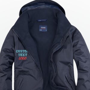 May include: A navy blue waterproof jacket with a hood and a full-length zip. The jacket has a high collar and the text "CUSTOM TEXT LOGO" in teal and red. Suitable for outdoor activities, it offers protection from wind and rain.