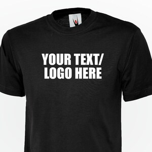 May include: A black short-sleeved t-shirt featuring the white text "YOUR TEXT/ LOGO HERE" printed across the chest. The garment has a crew neckline and a standard fit, showcasing a blank space intended for custom personalisation or branding.