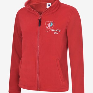 May include: A red fleece zip-up jacket with a high collar and two front pockets. The jacket features a heart-shaped graphic with baby footprints and the text "Kinsley RN". The zipper is black.
