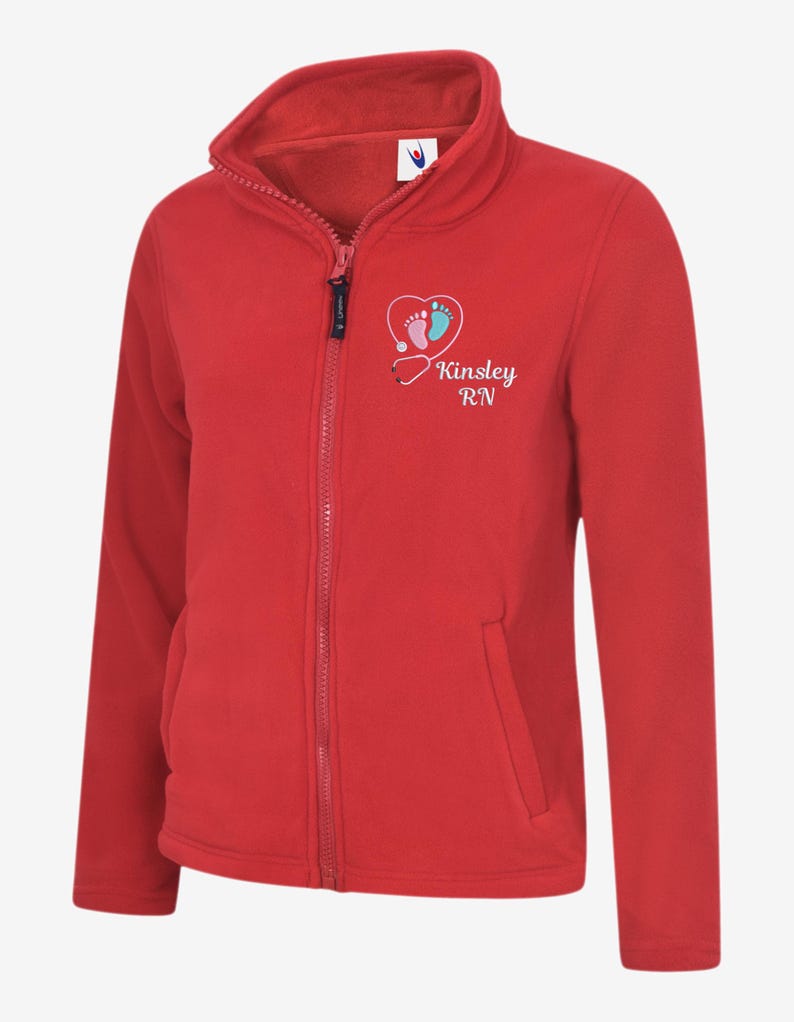 May include: A red fleece zip-up jacket with a high collar and two front pockets. The jacket features a heart-shaped graphic with baby footprints and the text "Kinsley RN". The zipper is black.