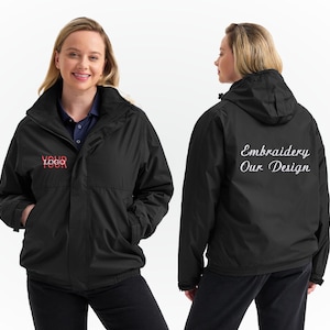 Può includere: Giacca nera con cappuccio e collo alto. La parte anteriore della giacca presenta la scritta "YOUR LOGO" in rosso. La parte posteriore della giacca presenta la scritta "Embroidery Our Design" in bianco. La modella indossa una camicia blu.