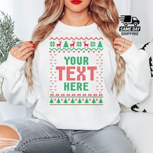 Peut inclure: Un sweat-shirt blanc à col rond orné d'un motif festif de Noël en rouge et vert. Le design comprend des rennes et des sapins entourant le texte centré YOUR TEXT HERE dans une impression graphique de style tricot pixélisé.