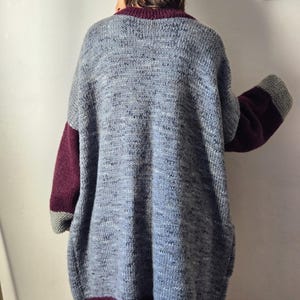 Puede incluir: Un c&aacute;rdigan de punto gris extragrande con mangas y ribetes burdeos. El c&aacute;rdigan tiene un aspecto texturizado y presenta un cuello y dobladillo burdeos oscuro. Las mangas tienen pu&ntilde;os grises. La prenda parece hecha a mano.