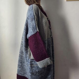 Puede incluir: Un c&aacute;rdigan largo y extragrande en tonos azul, gris y burdeos. El su&eacute;ter de punto presenta un dise&ntilde;o de bloques de color con mangas y ribetes burdeos. Tiene una parte delantera abotonada y dos bolsillos delanteros. El c&aacute;rdigan llega a la rodilla.