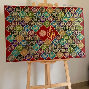 May include: A rectangular canvas art piece featuring Arabic calligraphy in gold lettering on a red background. The artwork is displayed on a wooden easel. The calligraphy is arranged in a grid pattern with various colors.
