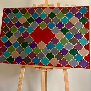 May include: A colorful abstract painting on a red background, featuring a geometric pattern of interlocking shapes in teal, purple, green, and gold. The artwork is displayed on a wooden easel.