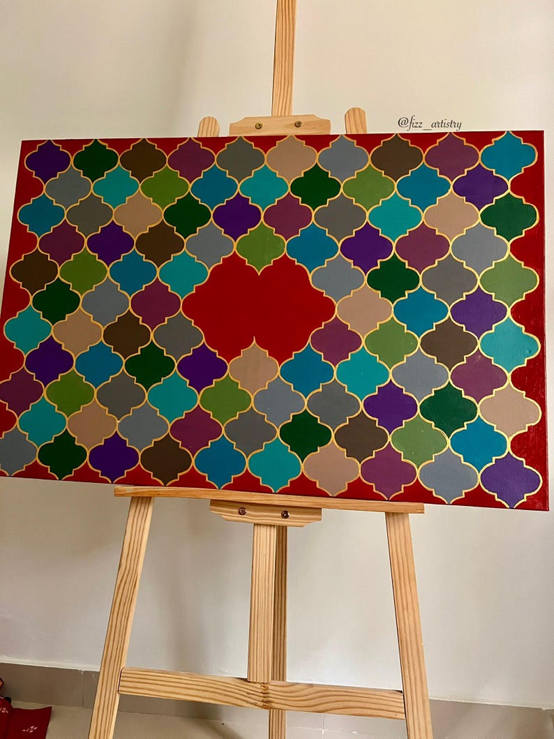 May include: A colorful abstract painting on a red background, featuring a geometric pattern of interlocking shapes in teal, purple, green, and gold. The artwork is displayed on a wooden easel.