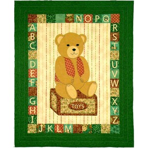May include: A rectangular quilt featuring a central tan teddy bear sitting on a box labeled TOYS. The bear wears a red patterned vest. The center panel has vertical stripes, surrounded by a border of alphabet letters A through Z in squares.