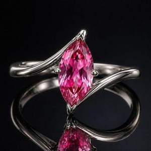 Puede incluir: Anillo de plata con una gema rosa en forma de marquesa. La banda del anillo tiene un diseño fluido y asimétrico. La gema está engastada en un engaste de garras, sobre un fondo negro.