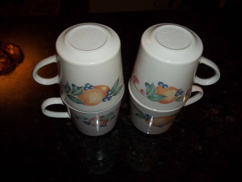 Puede incluir: Juego de cuatro tazas de cer&aacute;mica blanca con un dise&ntilde;o de frutas y flores. Las tazas est&aacute;n apiladas en pares.