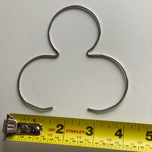 May include: A silver metal wire hanger with three loops, measuring approximately 4 inches in length.
