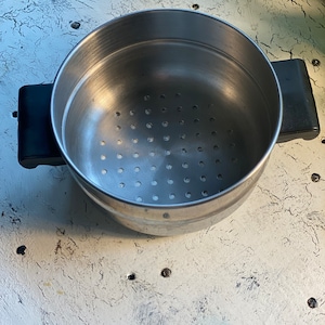 May include: A stainless steel steamer pot with a removable strainer insert. The pot has two black handles.