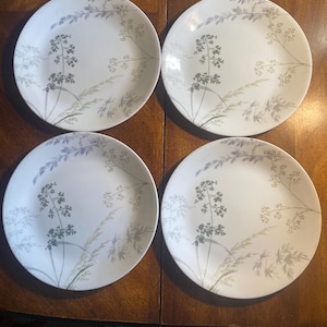 May include: A set of four round white dinner plates, each featuring a delicate botanical pattern of grey and light green grasses and wildflowers. The design is printed across the surface of the plates, showcasing slender stems and fine foliage.