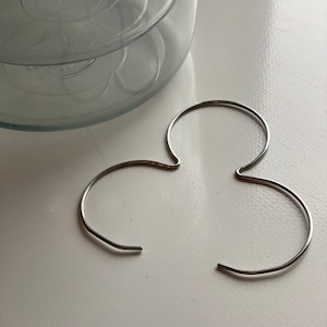 May include: A clear glass jar with a wide opening and a silver-colored metal ring. The ring is in the shape of a stylized clover. The jar is on a white surface.