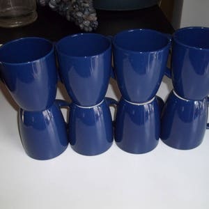 May include: Six dark blue ceramic mugs with rounded handles. The mugs are stacked in pairs.
