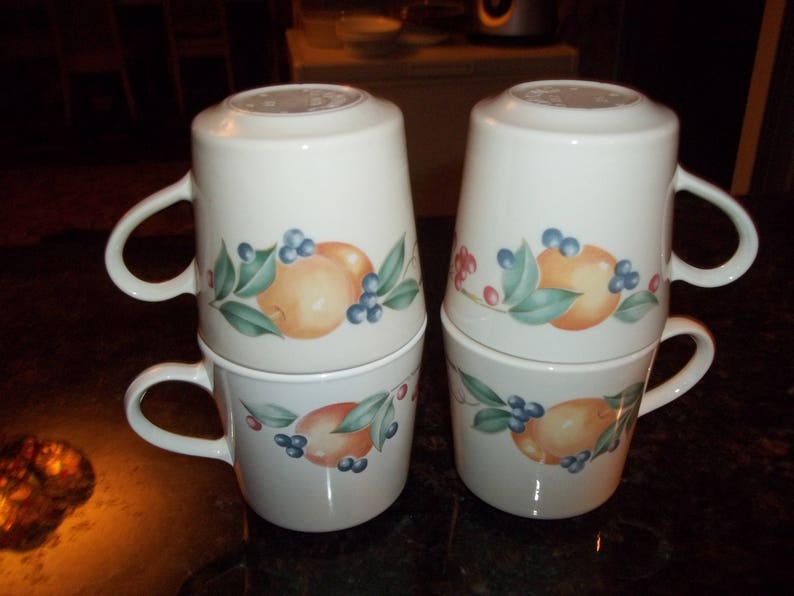 Puede incluir: Juego de cuatro tazas de cer&aacute;mica blanca con un dise&ntilde;o de frutas y flores. Cada taza presenta una fruta diferente, incluyendo naranjas, limones y limas. Las tazas tienen un fondo blanco con un dise&ntilde;o verde, amarillo y azul.