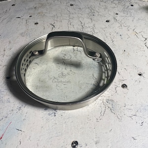 May include: A silver-colored Calphalon glass lid with a handle and a steam vent.