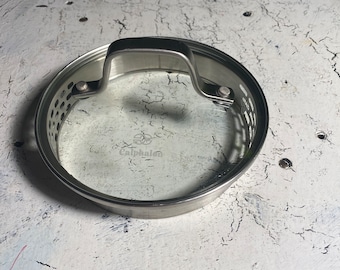 May include: A silver-colored Calphalon glass lid with a handle and a steam vent.
