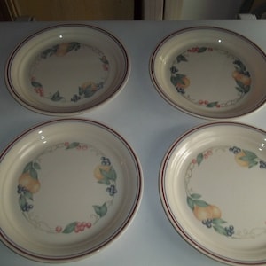 May include: Four white ceramic dinner plates with a red and blue rim. Each plate features a floral design with a vine of green leaves, yellow fruit, red berries, and blue flowers.