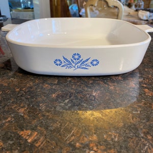 May include: White rectangular baking dish with blue floral design. The dish has two handles on the sides.