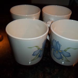 May include: Four white ceramic mugs with blue and green floral designs. The mugs have a rounded shape and a wide rim.