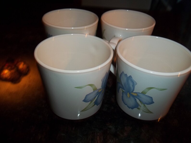 May include: Four white ceramic mugs with blue and green floral designs. The mugs have a rounded shape and a wide rim.