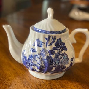 May include: A white teapot with a blue and white floral pattern. The teapot has a lid and a spout. The pattern is a traditional Chinese design.