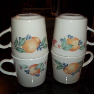 Puede incluir: Juego de cuatro tazas de cer&aacute;mica blanca con un dise&ntilde;o de c&iacute;tricos y bayas. Las tazas est&aacute;n apiladas en dos pares.