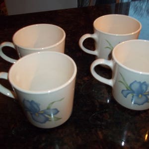 May include: Four white ceramic mugs with blue and green floral designs. The mugs have a simple, rounded shape and are perfect for everyday use.