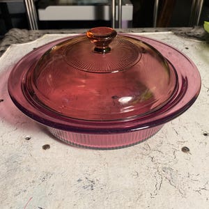 May include: A vintage pink glass baking dish with a lid. The dish has a fluted edge and a knob on the lid.