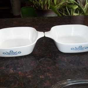 May include: Two white square baking dishes with blue floral designs. The dishes have handles on each side.