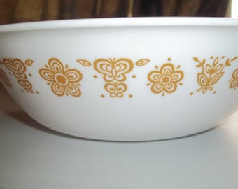 May include: White ceramic bowl with a gold floral pattern. The design includes stylized flowers and butterfly motifs. The bowl has a rounded shape and is suitable for serving food. A vintage kitchenware item.