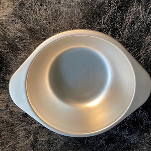 May include: A silver metal bowl with two handles. The bowl is empty and has a smooth, shiny surface.
