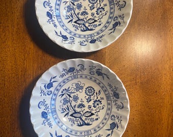 May include: Two round white ceramic bowls with scalloped edges, each featuring a detailed blue floral and botanical pattern in the center and along the inner rim, characterized by intricate stems, leaves, and stylized blossoms in a classic design.