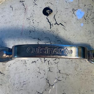 May include: Close-up of a Cuisinart pot lid. The lid is made of clear glass with a silver-colored handle. The handle has the Cuisinart logo. The glass has a distressed, crackled pattern.