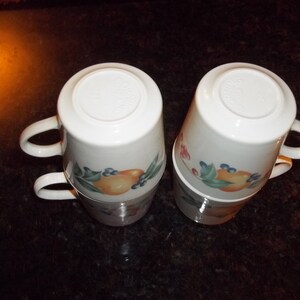 Puede incluir: Juego de cuatro tazas de cer&aacute;mica blanca con un dise&ntilde;o floral con frutas y bayas. Las tazas tienen una forma redondeada y un asa a cada lado.