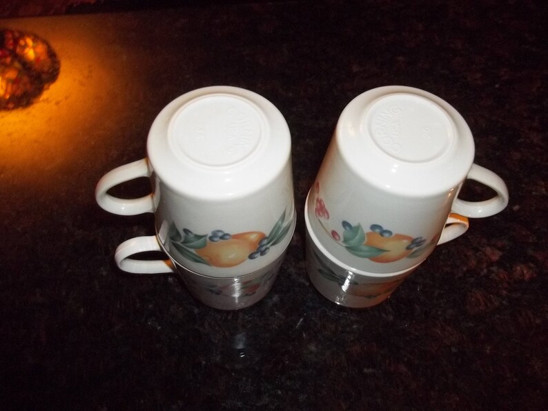 Puede incluir: Juego de cuatro tazas de cer&aacute;mica blanca con un dise&ntilde;o floral con frutas y bayas. Las tazas tienen una forma redondeada y un asa a cada lado.