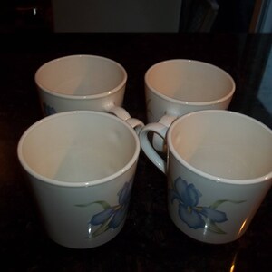 May include: Four white ceramic mugs with blue and green floral designs. The mugs have a rounded shape and a handle on the side.
