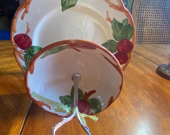 May include: A two-tiered ceramic serving stand featuring a cream-colored plate and bowl decorated with hand-painted red apples and green leaves. The tiers are connected by a central silver-toned metal handle with a decorative loop.