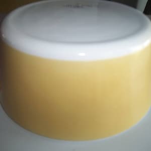 May include: A yellow and white Pyrex baking dish with a rounded shape and two handles. The dish is made of glass and has a white interior.