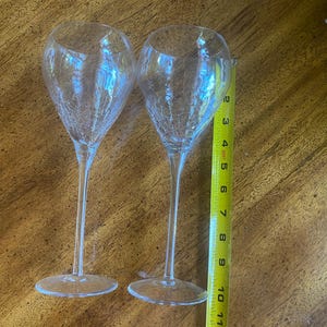 May include: Two clear, stemmed wine glasses with a crackle design. The glasses are approximately 10 inches tall. The glasses are on a wooden surface. A yellow measuring tape is next to the glasses.