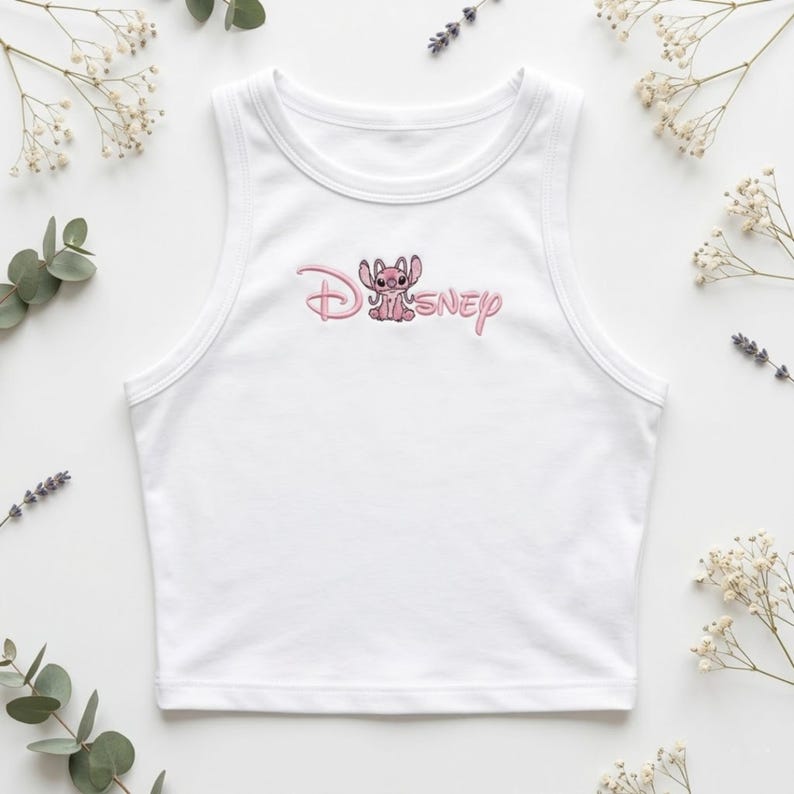 May include: White tank top with a pink embroidered Disney Stitch design. The design features the word "Disney" in a cursive font with a cartoon Stitch character. The top is sleeveless and has a rounded neckline.
