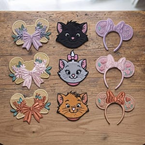 May include: A collection of nine embroidered patches arranged in three rows. The left column features three mouse-ear shaped patches with floral designs and bows. The center column shows three cat face patches. The right column displays three mouse-ear headbands.