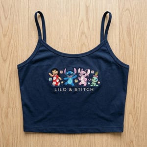 May include: Navy blue camisole top with an embroidered design of Lilo & Stitch characters. The design includes Lilo, Stitch, Angel, and a green alien. The words "LILO & STITCH" are embroidered below the characters.