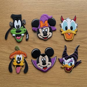 Könnte beinhalten: Sechs bestickte Charakter-Aufnäher: Goofy als Monster, Minnie Maus mit violettem Hexenhut, Donald Duck mit roten Hörnern, Pluto mit Kürbishut, Mickey Maus als Vampir und Maleficent mit ihren charakteristischen schwarzen Hörnern.