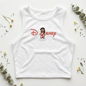 May include: White tank top with a red and pink Disney logo featuring a cartoon character. The sleeveless top is made of a soft material and is suitable for casual wear.